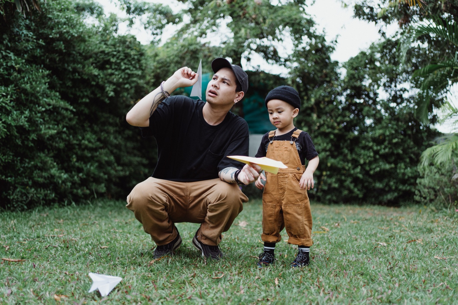 A dad and his little one flying paper planes in the garden