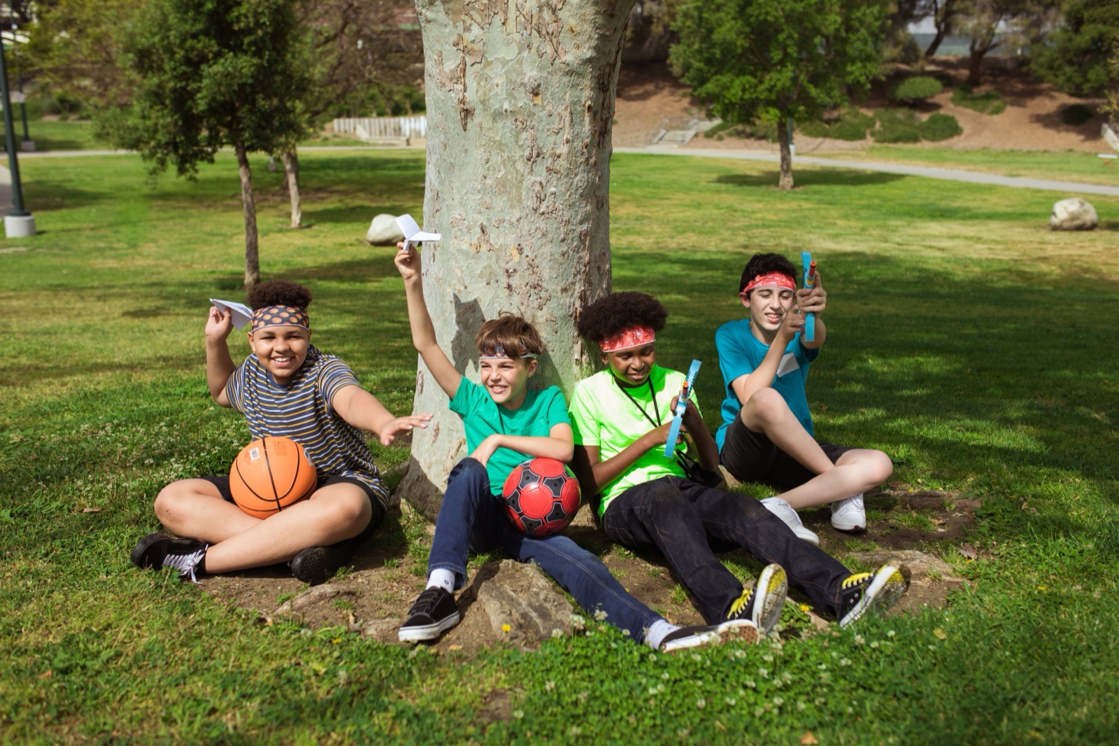 Four kids in a park holding their paper airplanes
