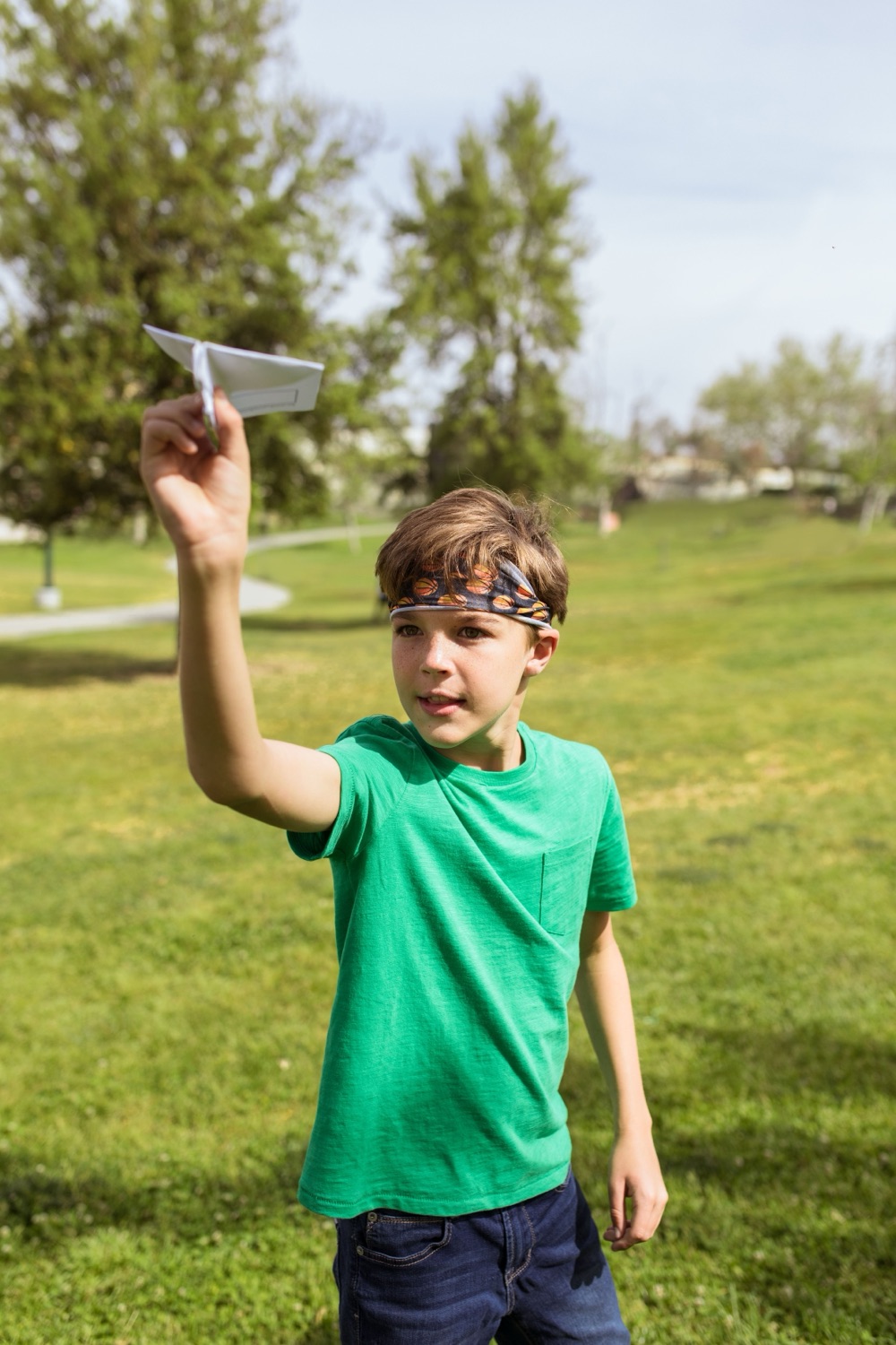 A boy holding up his paper airplane, ready to launch it in the park